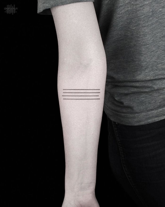 Minimalist geometric tattoo by Turkish artist Okan Uçkun featuring three parallel lines on a person's forearm.