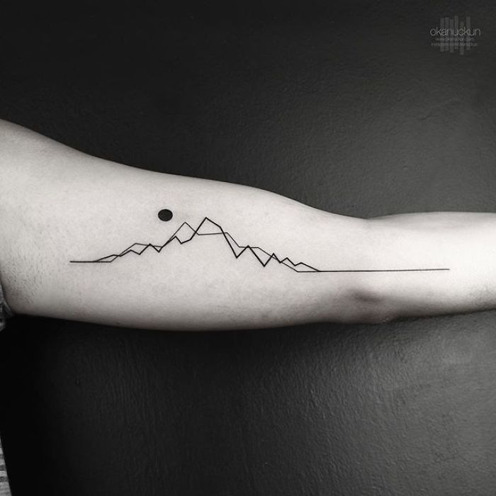 Minimalist geometric tattoo on arm by Turkish artist Okan Uçkun, featuring mountains and a dot.