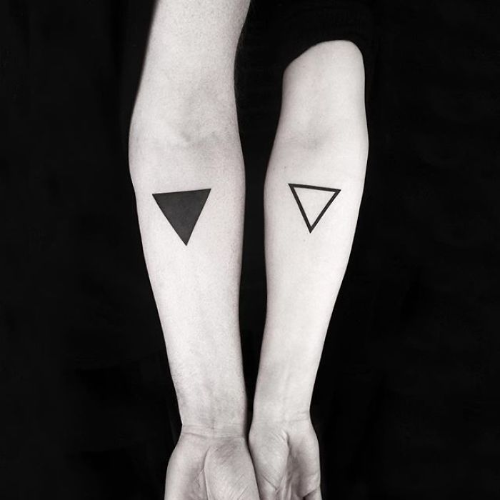 Geometric tattoos on forearms by Turkish artist, featuring solid and outlined triangles in black ink.