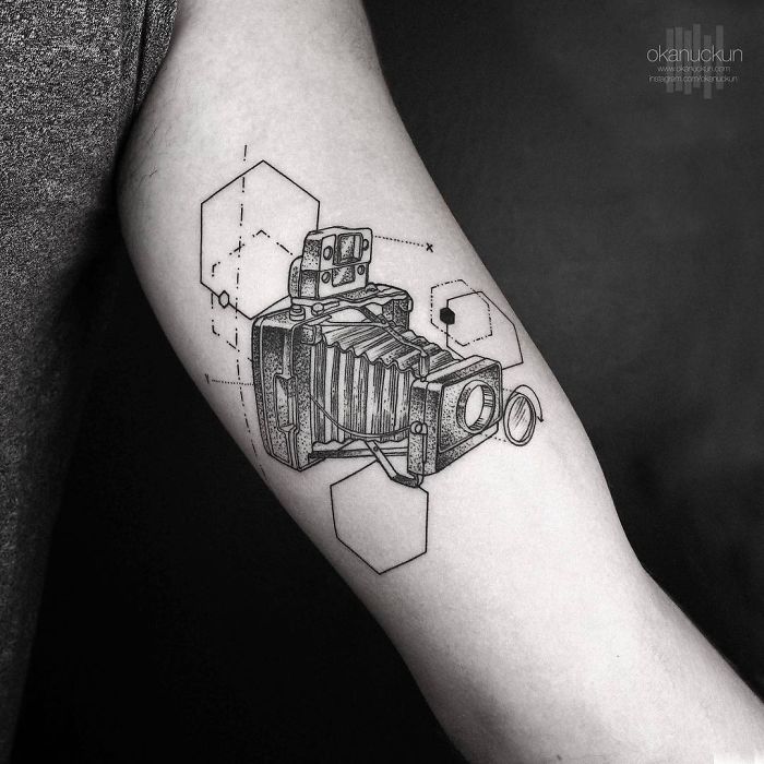 Geometric tattoo by Turkish artist Okan Uçkun on an arm, featuring a detailed camera design with hexagonal shapes.