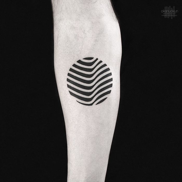 Geometric tattoo by Turkish artist Okan Uçkun featuring a black circular design with wavy lines on the forearm.