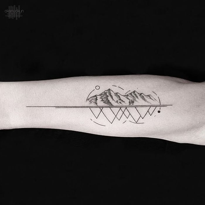 Geometric tattoo on forearm by Turkish artist Okan Uçkun, featuring mountains and abstract shapes.