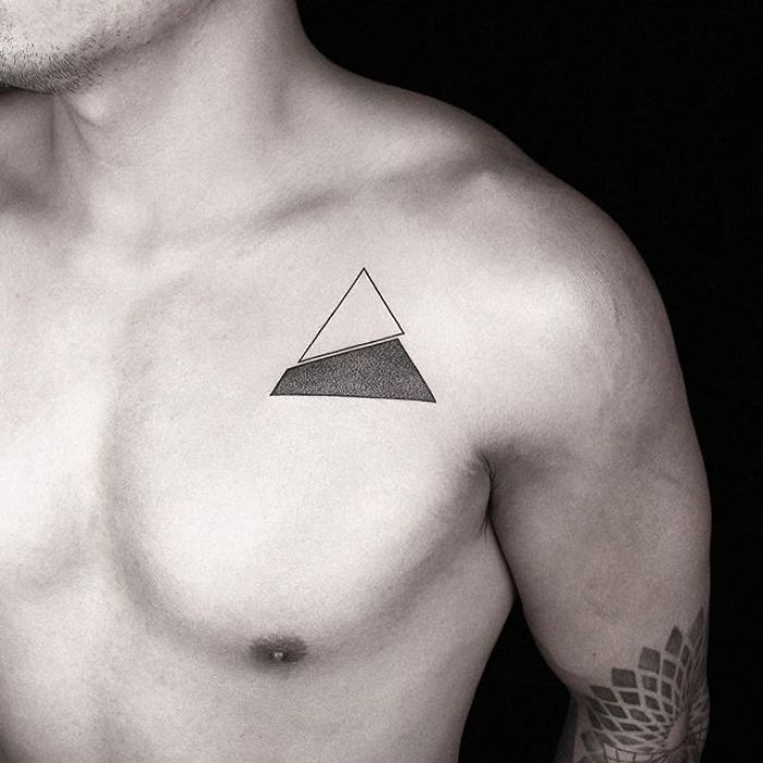 Geometric tattoo by Turkish artist Okan Uçkun on a person's chest, featuring a triangle design.