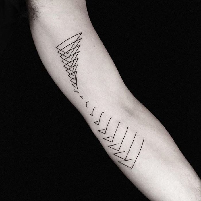 Arm showcasing a geometric tattoo design by Turkish artist Okan Uçkun, featuring abstract triangular shapes.
