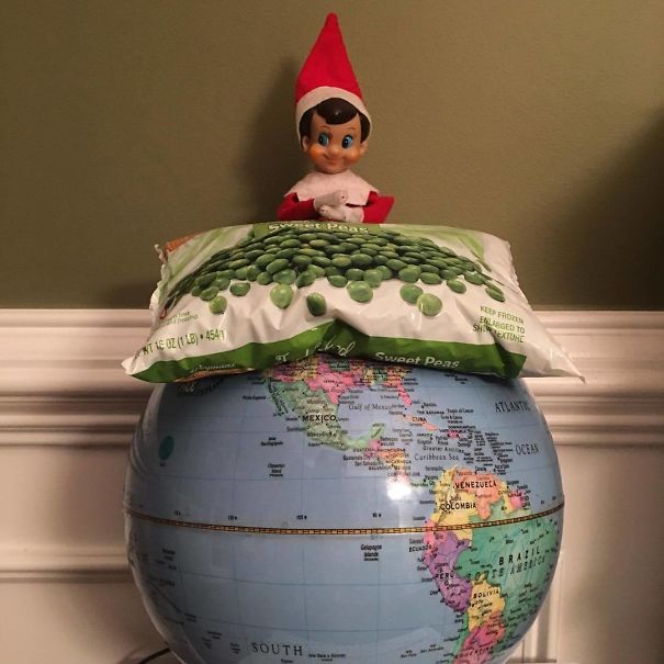 "Elf On The Shelf idea with elf sitting on a globe, resting on a bag of frozen peas, humorously representing 'world peace.'"