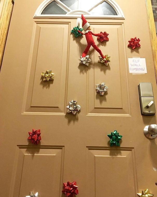 "Elf On The Shelf idea with the elf climbing a door using colorful gift bows as footholds, with a sign saying 'Elf Wall Climbing!'"