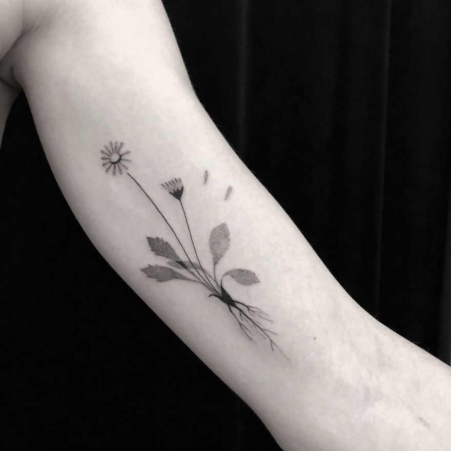 Minimalist botanical tattoo design featuring a delicate flower and leaves on an arm.