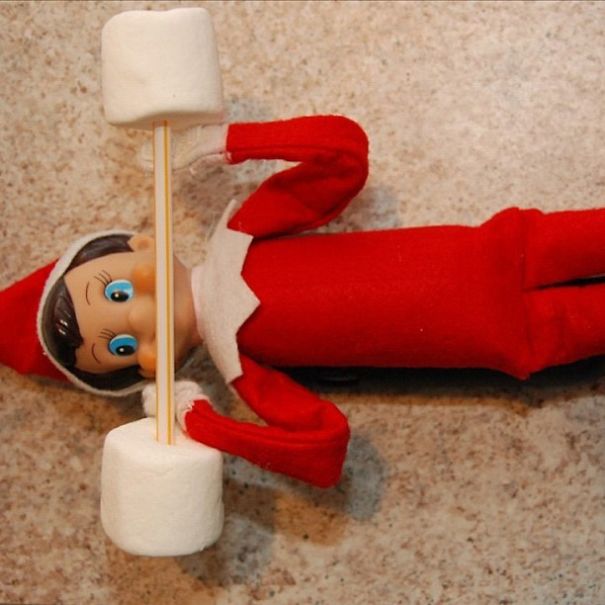 "Elf On The Shelf idea with the elf lifting a 'barbell' made of marshmallows on a stick, creating a playful weightlifting scene."