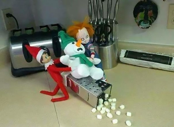 "Elf On The Shelf idea with the elf and a Chucky doll 'grating' a snowman toy over a cheese grater, spilling marshmallows onto the counter."