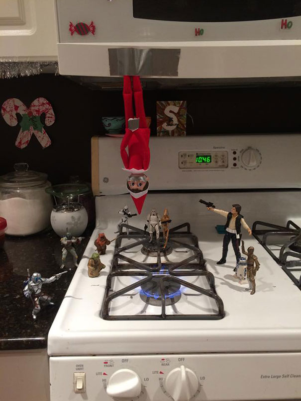 "Elf On The Shelf idea with the elf hanging upside down above a stovetop, surrounded by Star Wars action figures in a battle scene."