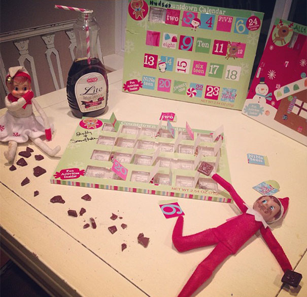 "Elf On The Shelf idea with two elves raiding an advent calendar, with chocolate pieces scattered around and one elf holding a bottle of syrup."
