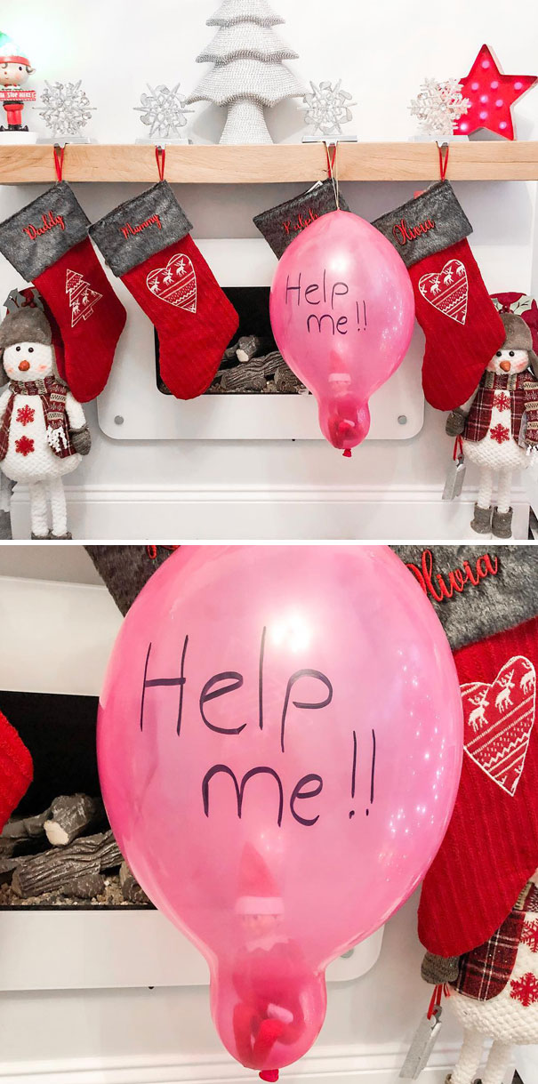 "Elf On The Shelf idea with the elf trapped inside a pink balloon labeled 'Help me!!' hanging by Christmas stockings on a mantel."