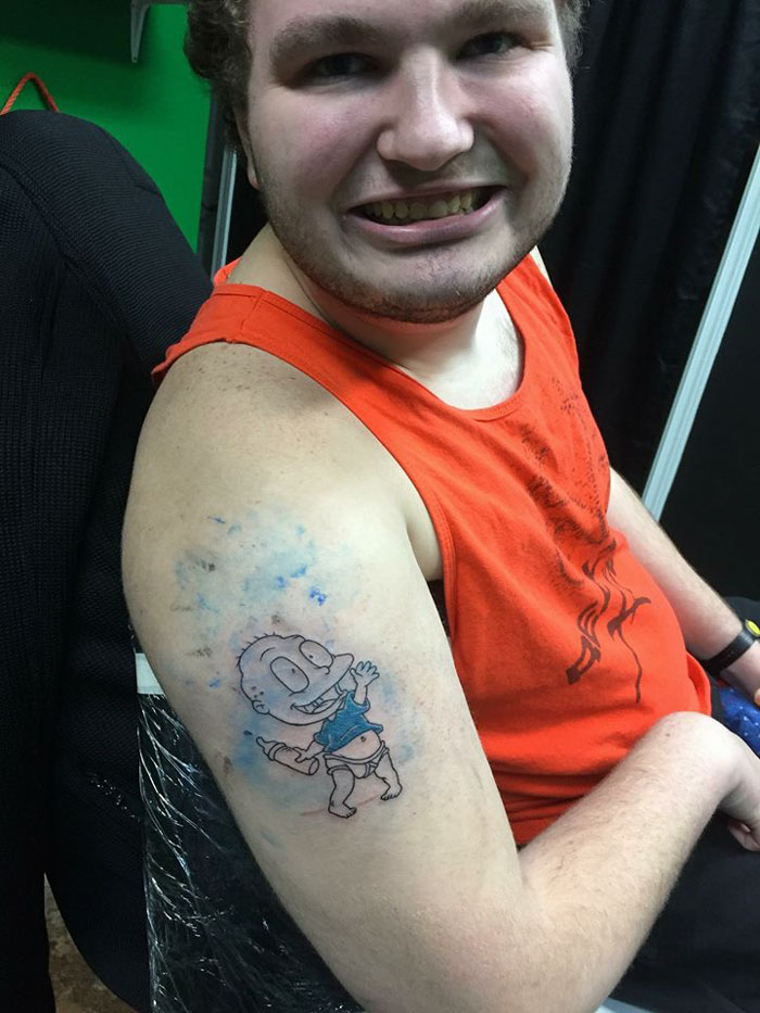 Autistic man proudly reveals new tattoo featuring a cartoon character on his arm, wearing an orange tank top. Autistic man proudly reveals new tattoo featuring a cartoon character on his arm, wearing an orange tank top.