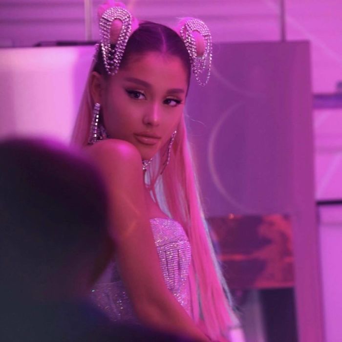 Ariana Grande in a sparkly outfit under pink lighting, with pearl hair accessories. Ariana Grande in a sparkly outfit under pink lighting, with pearl hair accessories.