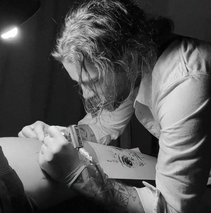 Artist meticulously tattooing a design under lamp light, part of a motion tattoo project. Artist meticulously tattooing a design under lamp light, part of a motion tattoo project.