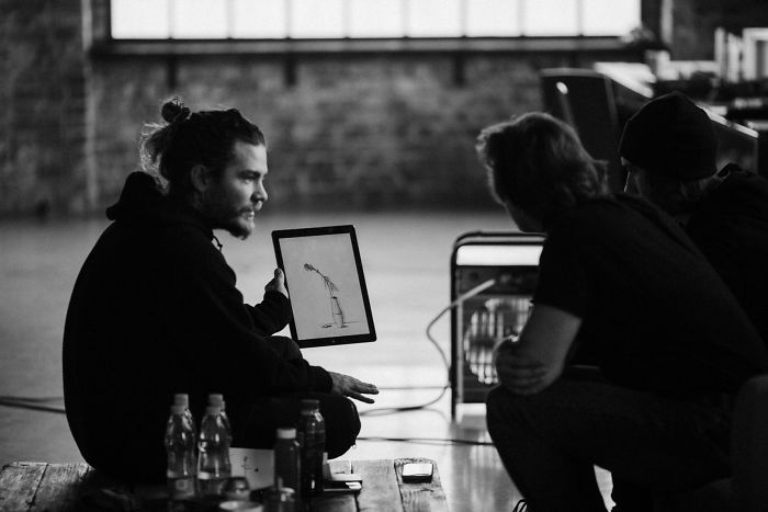 Artist discusses motion tattoo frames with two people, showing a digital sketch on a tablet. Artist discusses motion tattoo frames with two people, showing a digital sketch on a tablet.