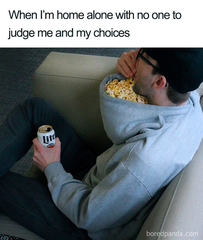 Man in gray hoodie eating popcorn from hood, holding a drink, with text about being home alone. Weight loss and diet meme.