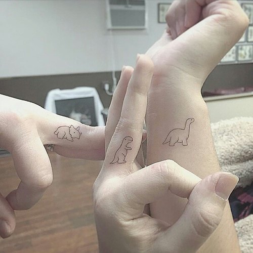Three hands display minimalist dinosaur finger tattoos, showcasing the latest trend in body art.