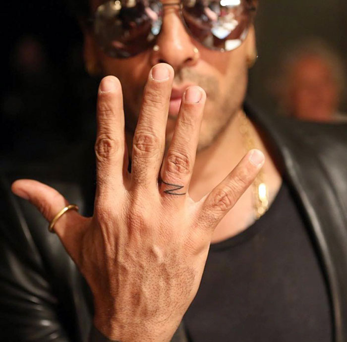 Man showcasing finger tattoo design while wearing sunglasses and a black jacket.