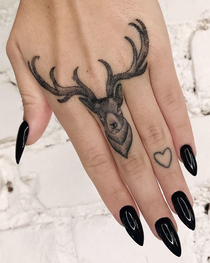 Deer and heart finger tattoos with black nail polish on a hand.