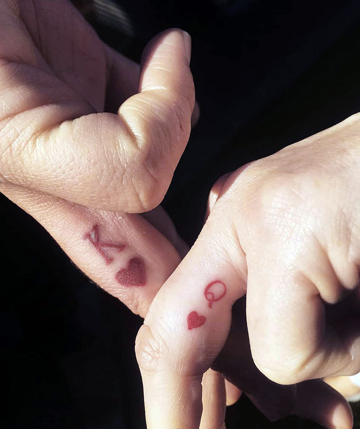 Close-up of hands showing finger tattoos with red hearts and letters, highlighting latest trend in ink art.