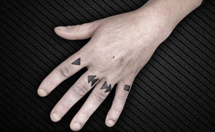Geometric finger tattoos on a hand, showcasing the newest trend in tattoo design on a textured black background.