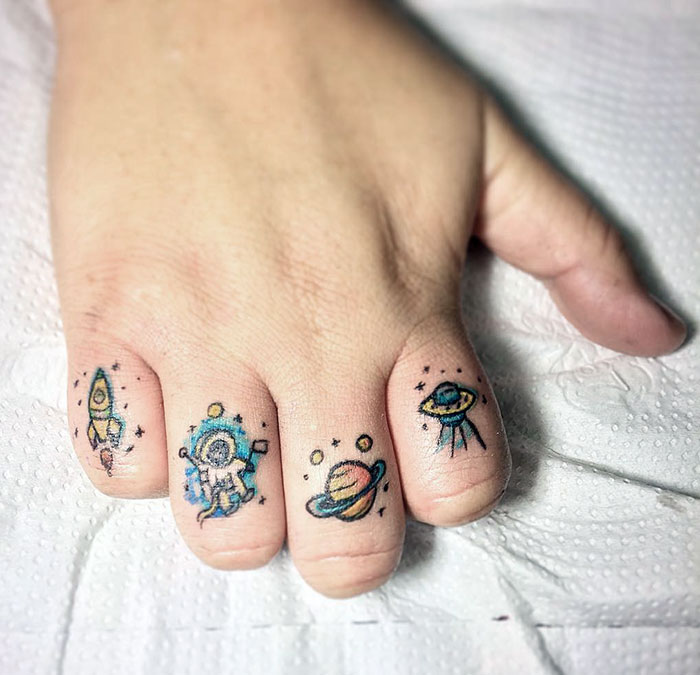 Cute astral-themed finger tattoos showing a rocket, astronaut, planet, and UFO, showcasing the latest tattoo trends.
