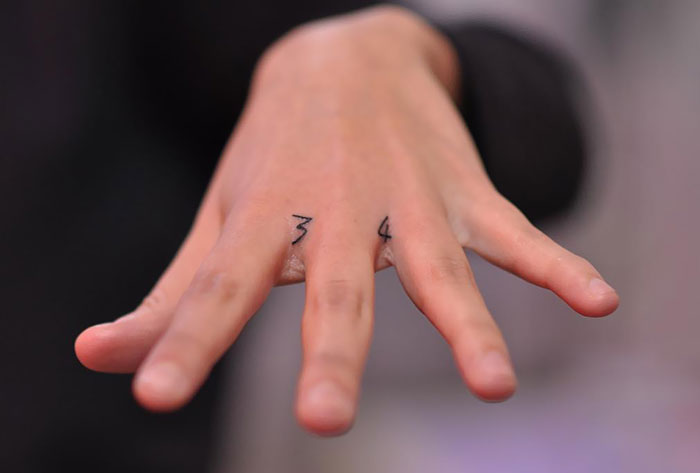 Close-up of finger tattoos on a hand, featuring simple numbers as part of the latest trend in finger tattoo designs.