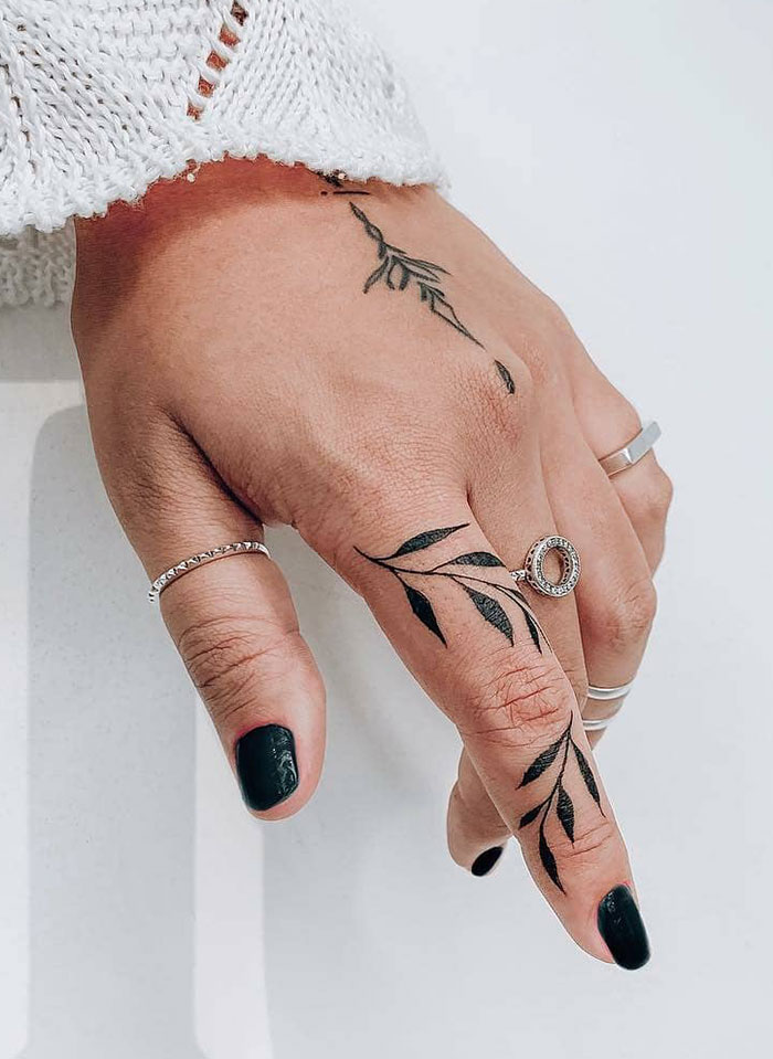 Close-up of finger tattoos featuring leaf designs, complemented by black nail polish and silver rings.