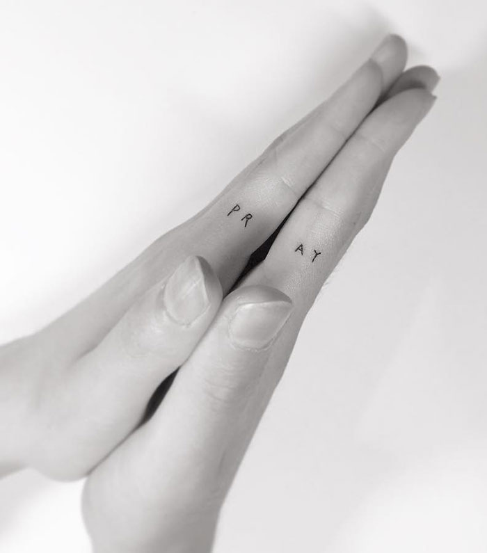 Close-up of fingers with "PRAY" tattoo, showcasing newest trend in finger tattoos.