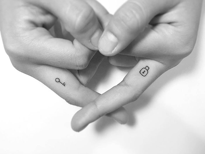 Close-up of small finger tattoos featuring a key and lock, showcasing trendy ink ideas.