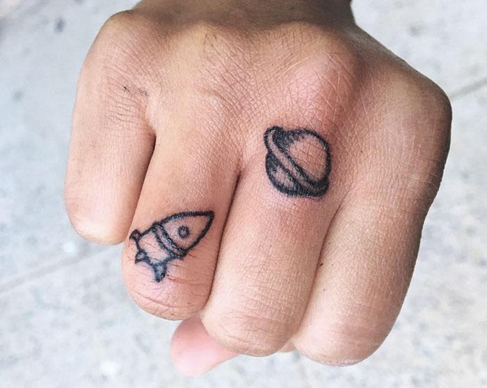 Finger tattoos featuring a rocket and planet design with fine details.