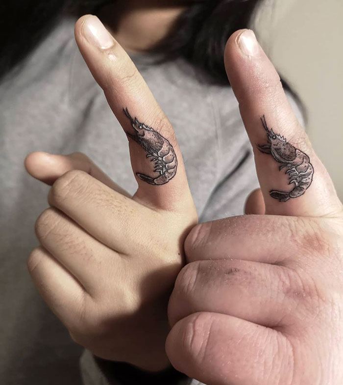 Close-up of unique finger tattoos featuring shrimp designs on two thumbs.