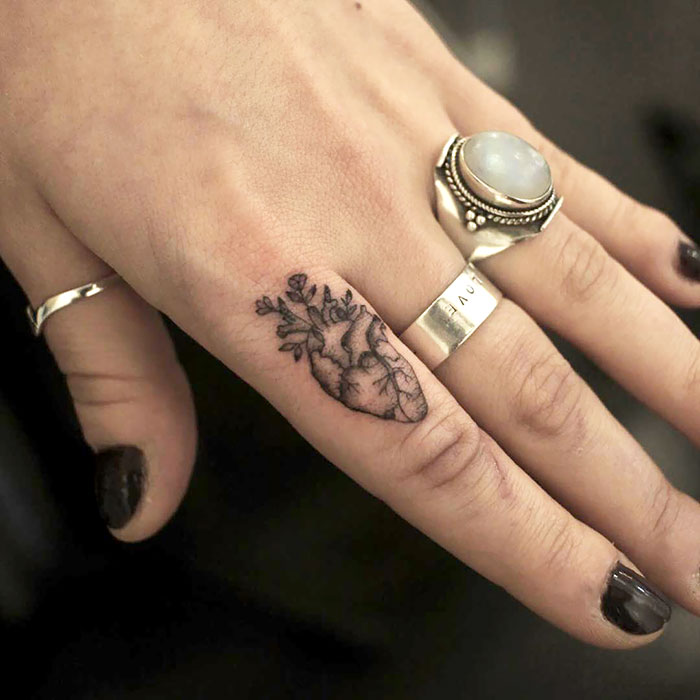 Finger tattoo featuring a heart design with branches, complemented by stylish rings; a trendy choice for tattoo enthusiasts.