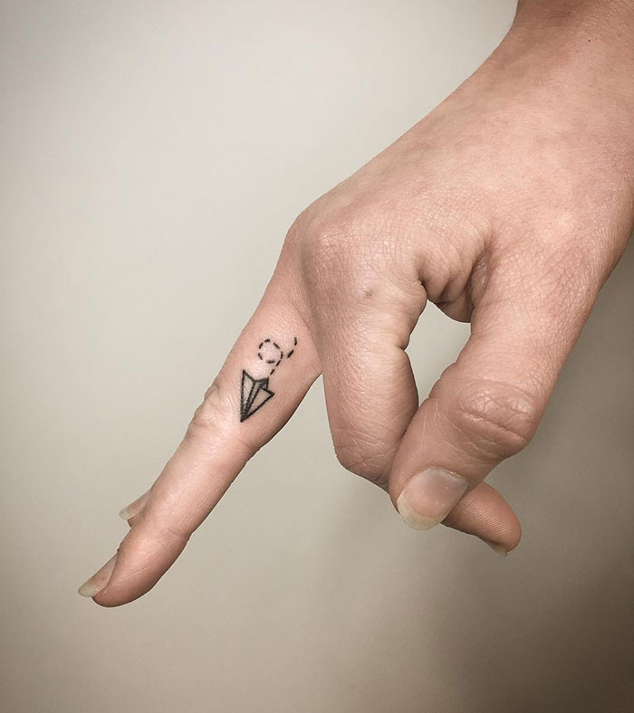 Minimalist finger tattoo featuring a paper airplane outline on a person's finger.