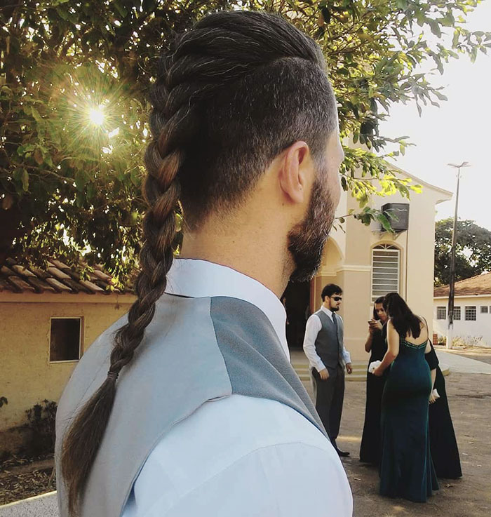 Man with a braided Viking hairstyle, wearing a vest, outside at an event, embodying modern-day fierce Viking looks.