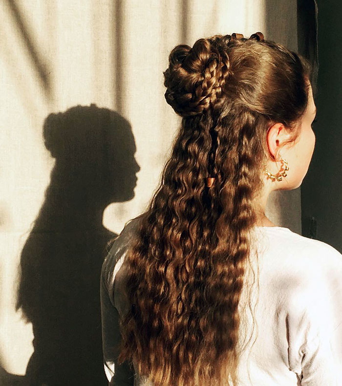 Modern Viking hairstyle with intricate braided bun and wavy hair, casting a shadow on the wall.