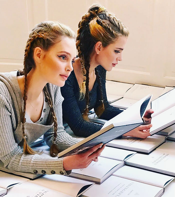 Two women with fierce Viking hairstyles, braided and stylish, reading books in a modern setting.