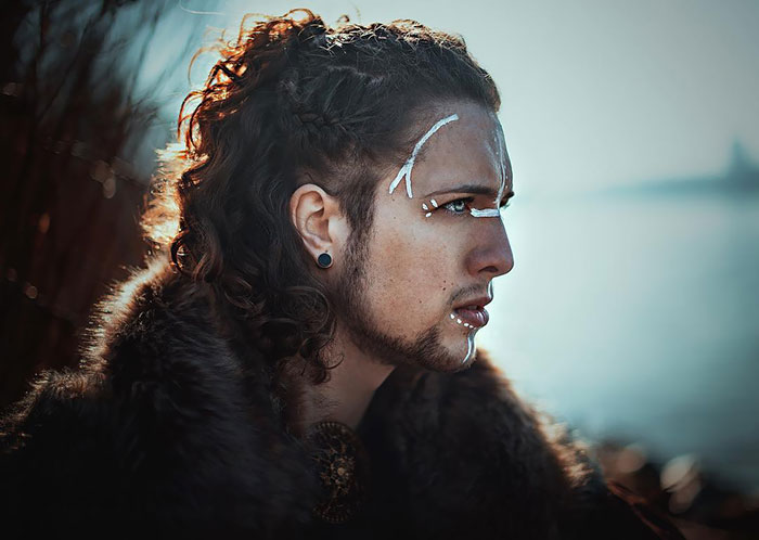 Person with fierce Viking hairstyle and face paint, wearing fur, gazing into the distance with determination.