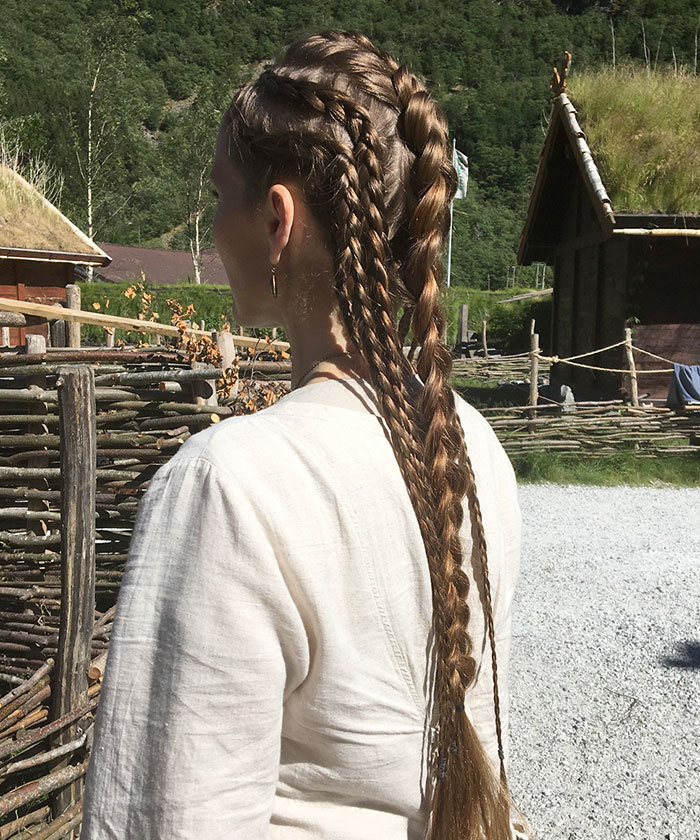 Woman with intricate Viking hairstyles, braids cascading down her back, showcasing fierce Nordic style.
