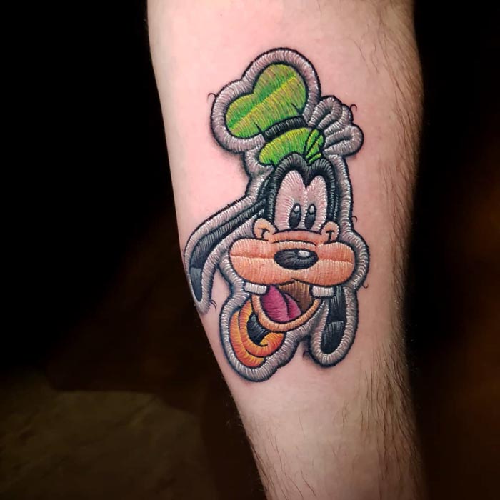 Embroidery tattoo featuring a cartoon character on an arm by a Brazilian tattoo artist.