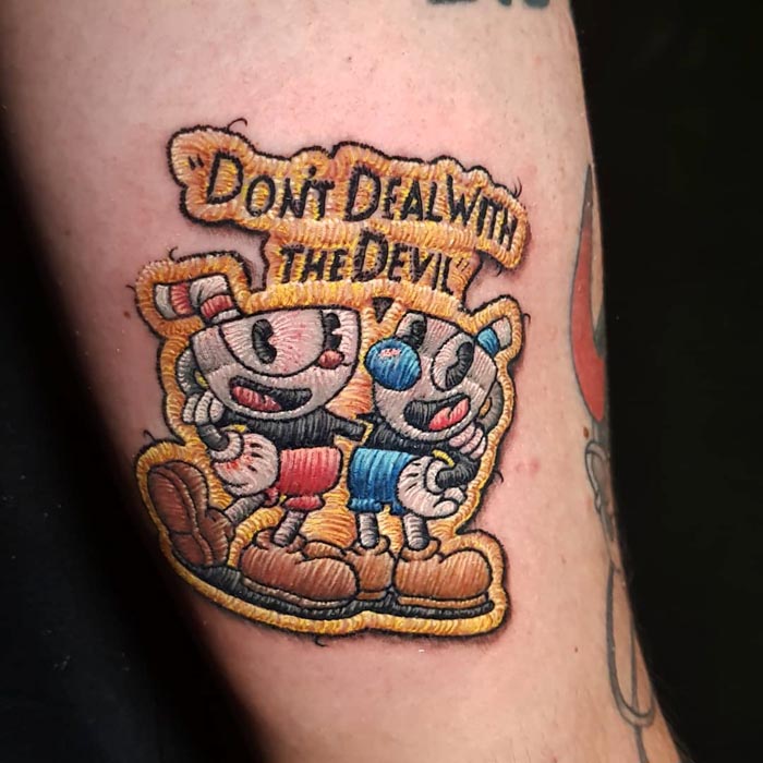 Embroidery tattoo on arm featuring cartoon characters and text, showcasing Brazilian tattoo artistry.