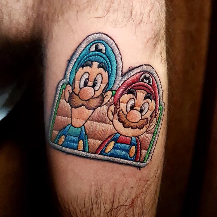 Embroidery tattoo of two iconic game characters on a forearm, showcasing Brazilian tattoo artist's unique style.