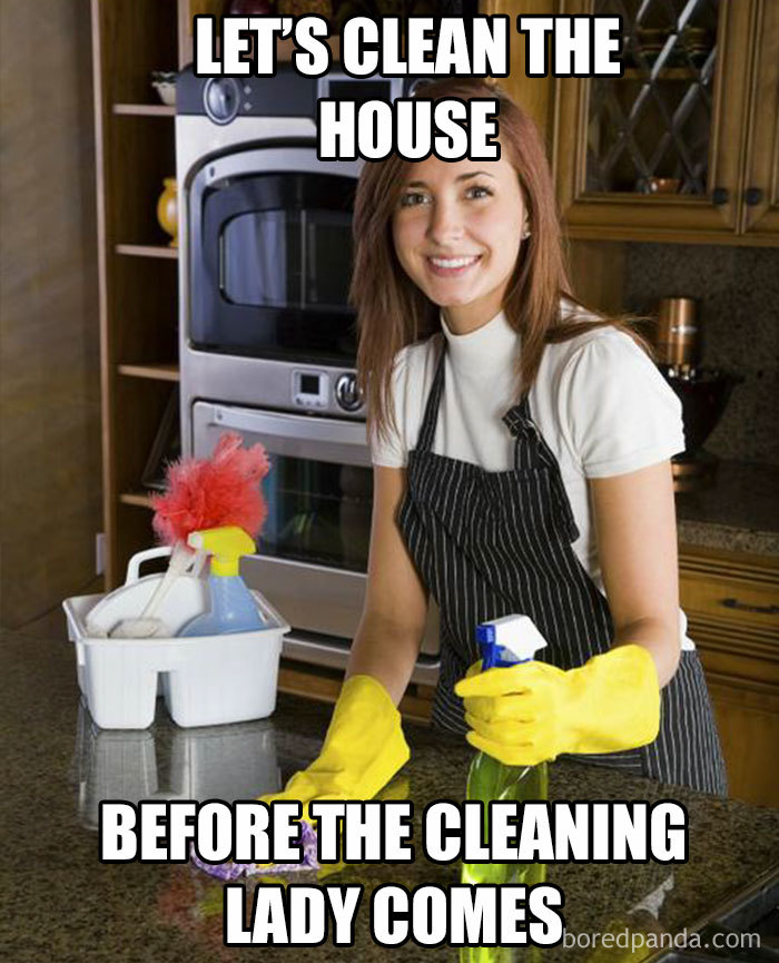 Woman in kitchen wearing gloves preparing to clean, with cleaning supplies on the counter.