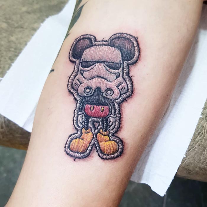 Embroidery tattoo featuring a stitched cartoon character on an arm, highlighting Brazilian tattoo artistry.
