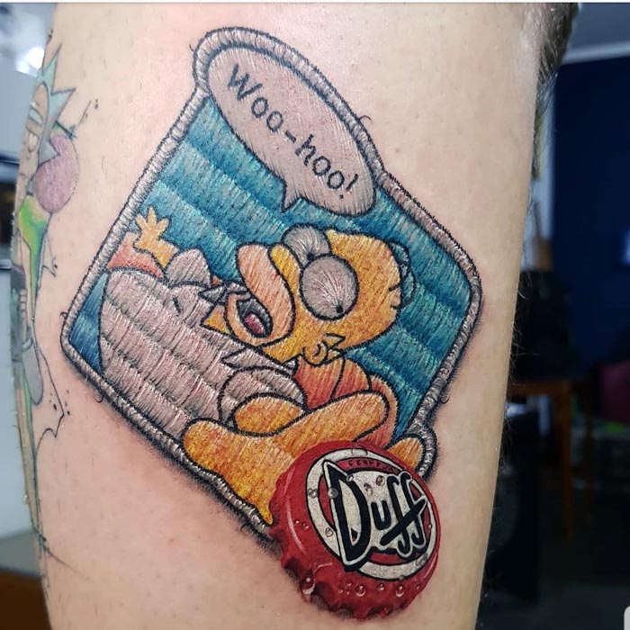 Embroidery tattoo of a cartoon character with "Woo-hoo!" speech bubble, detailed with a red bottle cap design.