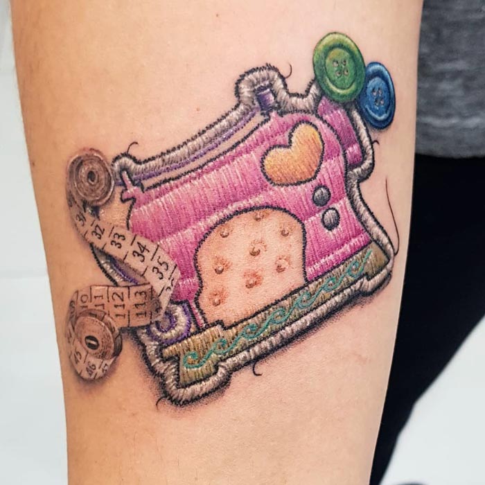 Embroidery-inspired tattoo of a pink sewing machine with buttons and measuring tape by Brazilian tattoo artist.
