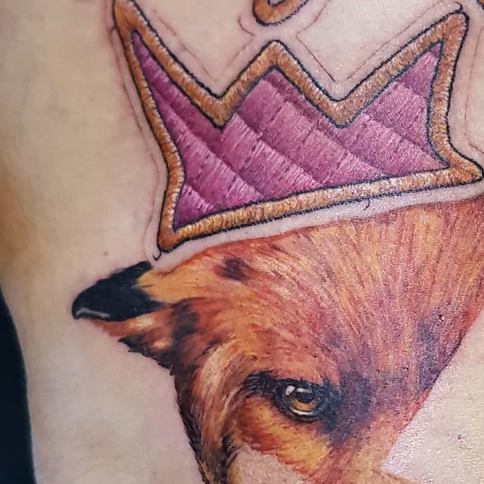 Embroidery tattoo of a purple crown and animal head by Brazilian artist.