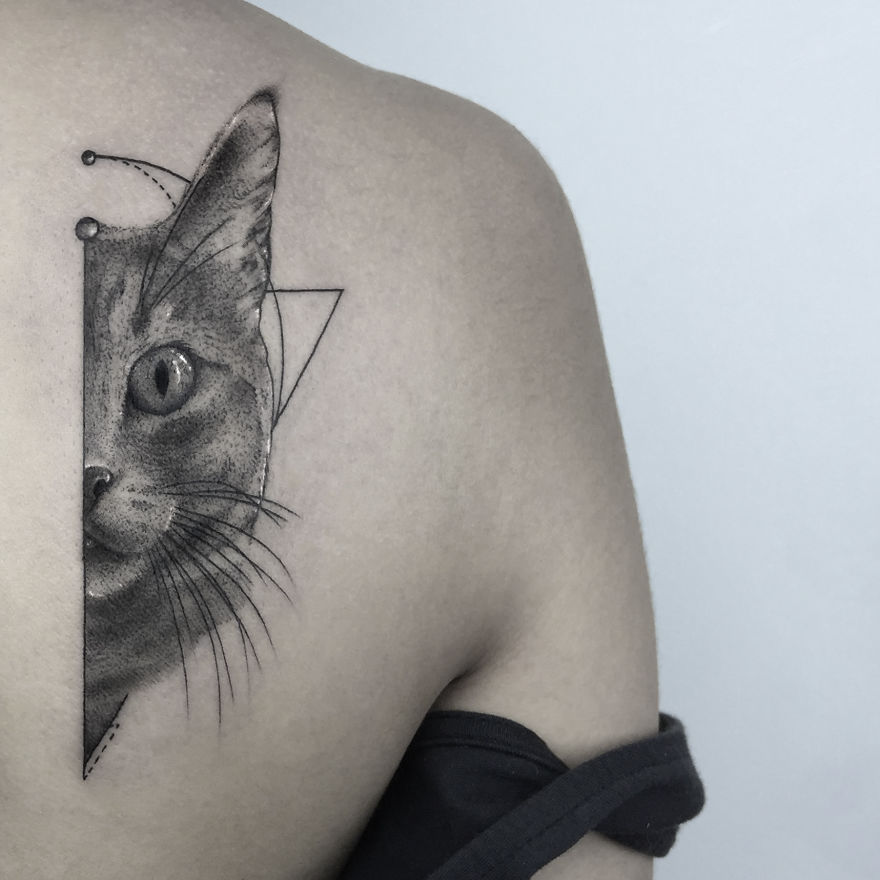 Geometric tattoo design of a cat on a person's shoulder, featuring triangles and circles in monochrome.
