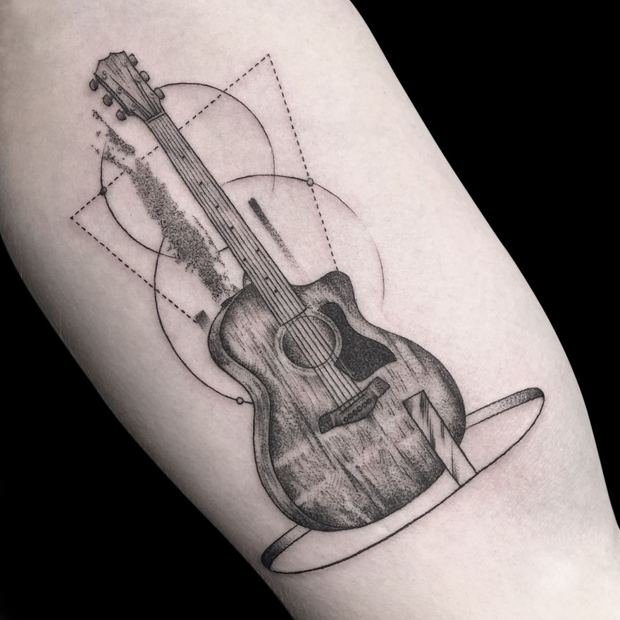Geometric tattoo design of a guitar with circles and lines on an arm.